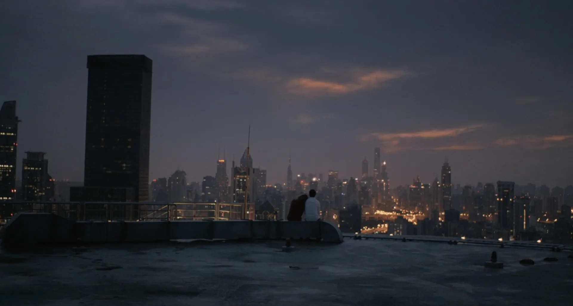 Dos figuras de espaldas miran la ciudad de noche desde una azotea, escena final de la película Her