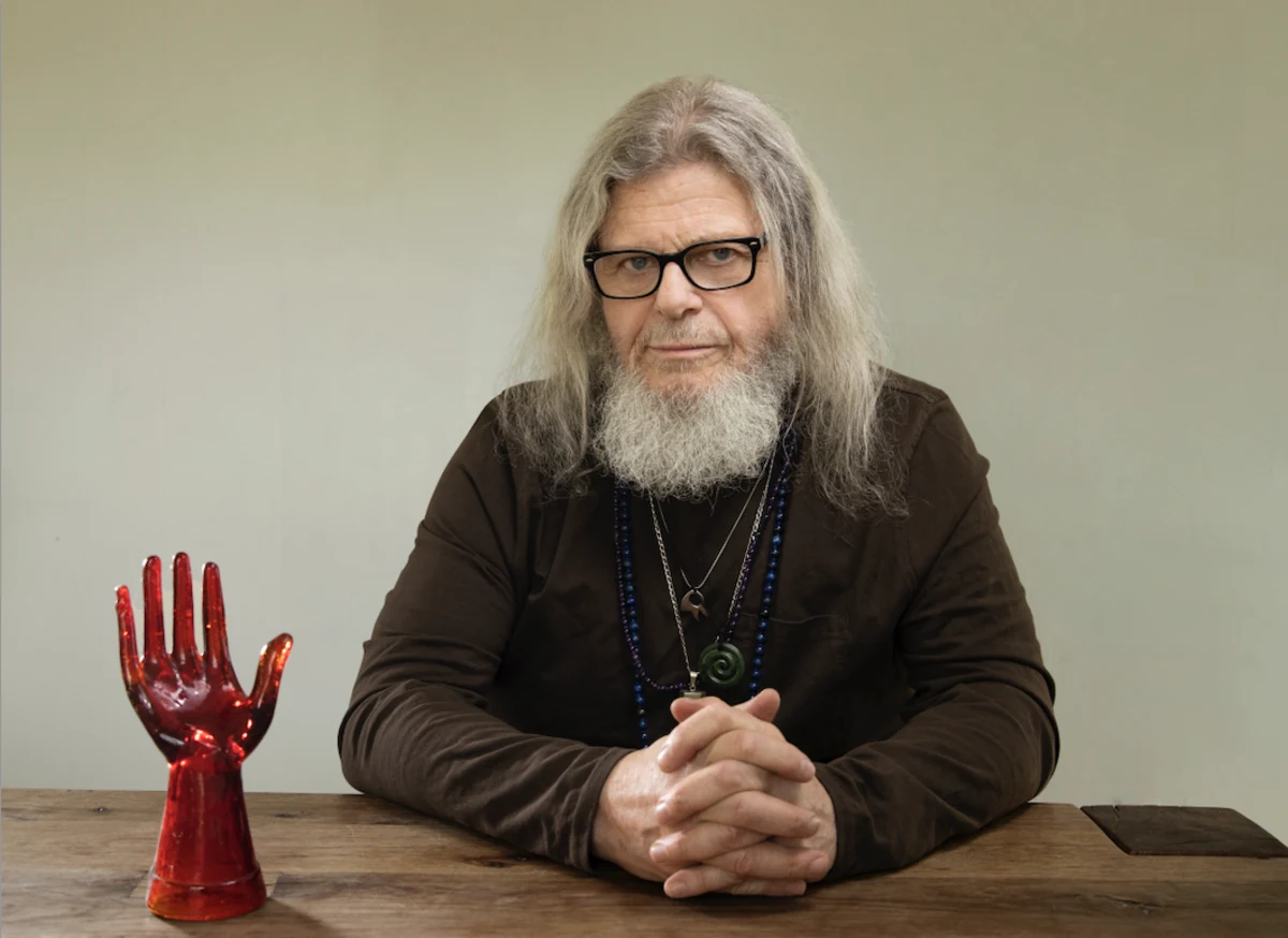 Gustavo Santaolalla retrato sobrio con manos cruzadas y mano roja escultórica