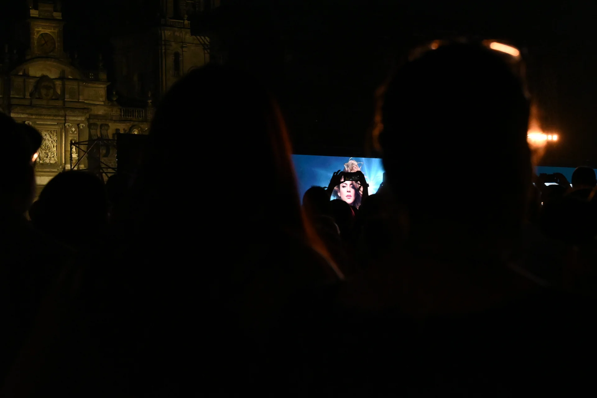 Siluetas del público viendo la pantalla del escenario con la Catedral Metropolitana iluminada al fondo durante el concierto de noche